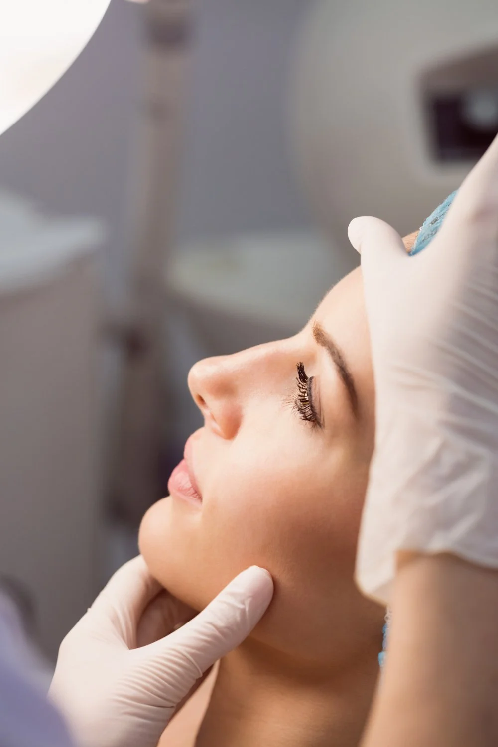 Mulher deitada recebendo um procedimento estético facial, com olhos fechados e expressão relaxada, enquanto um profissional de luvas realiza o procedimento.
