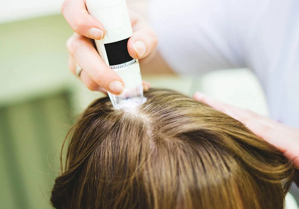 Médico aplicando um medicamento ou vacina na cabeça de uma pessoa com cabelo castanho.