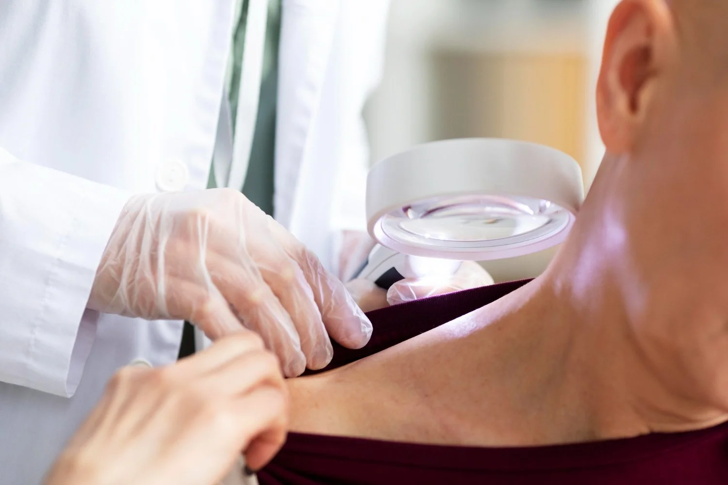 Profissional de saúde usando luvas, examinando o braço de uma pessoa com um dispositivo de luz, possivelmente para testes de diagnóstico, em ambiente clínico.