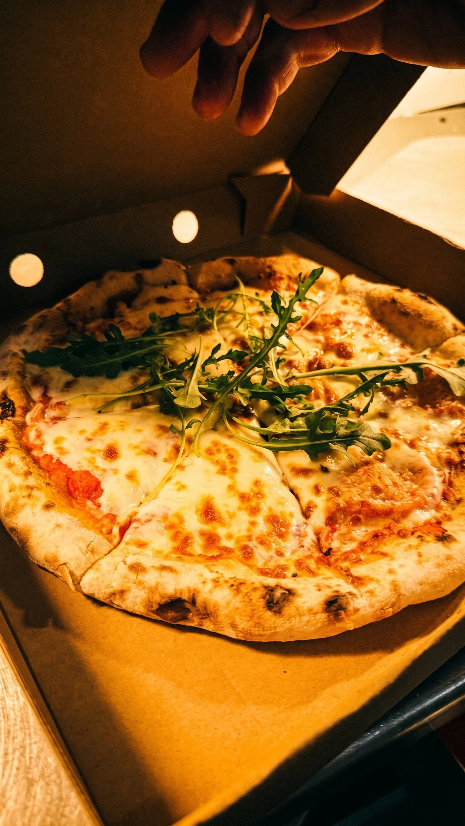 A pizza with cheese, tomato sauce, and arugula in an open pizza box.