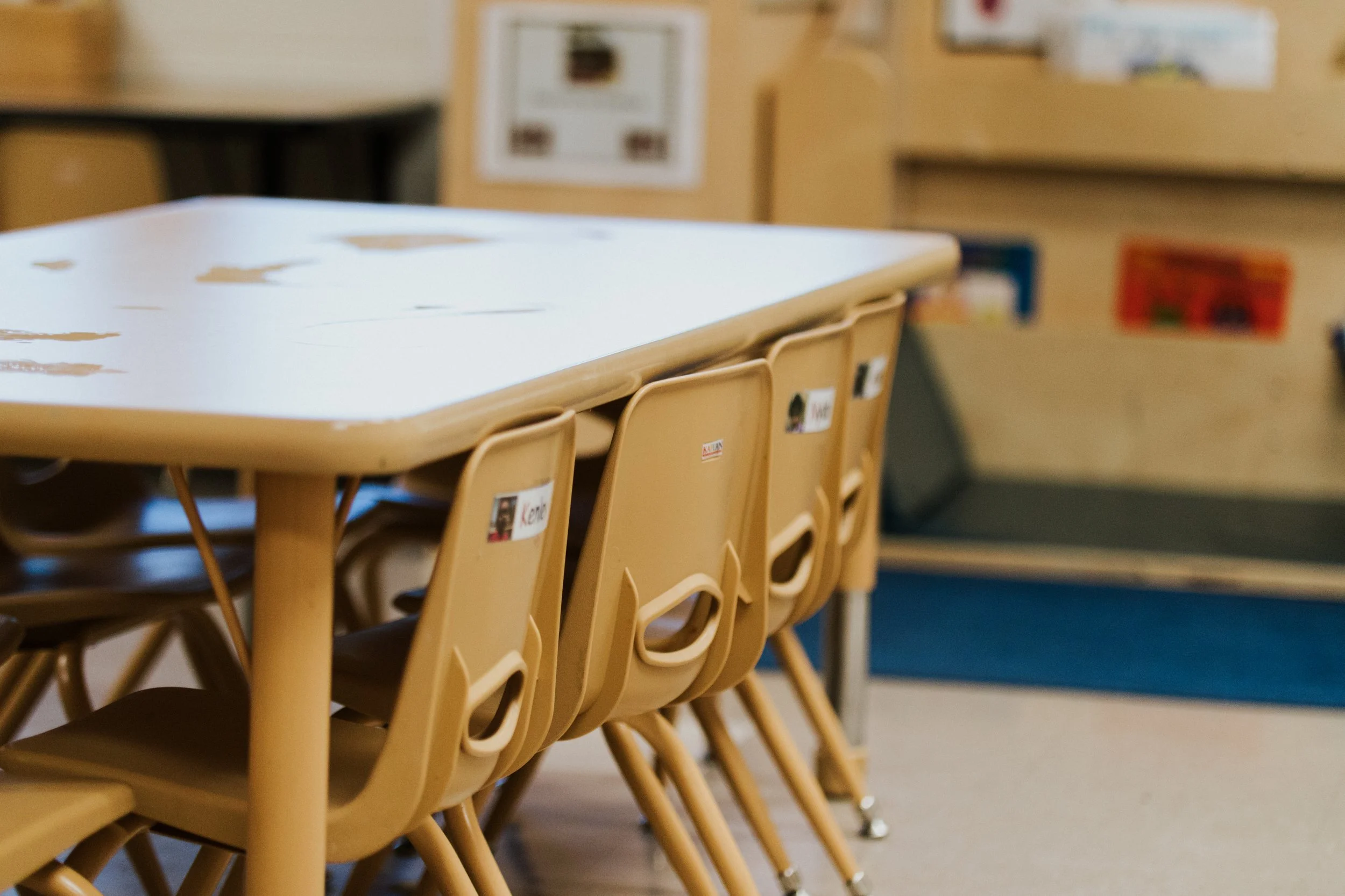 A row of stacked beige chairs with black seats in a classroom or school setting.