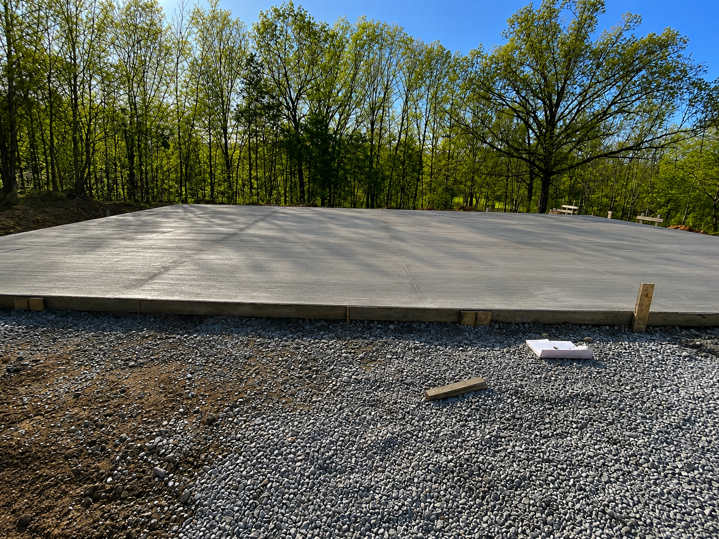 Newly poured concrete slab on a construction site surrounded by trees in a forested area.