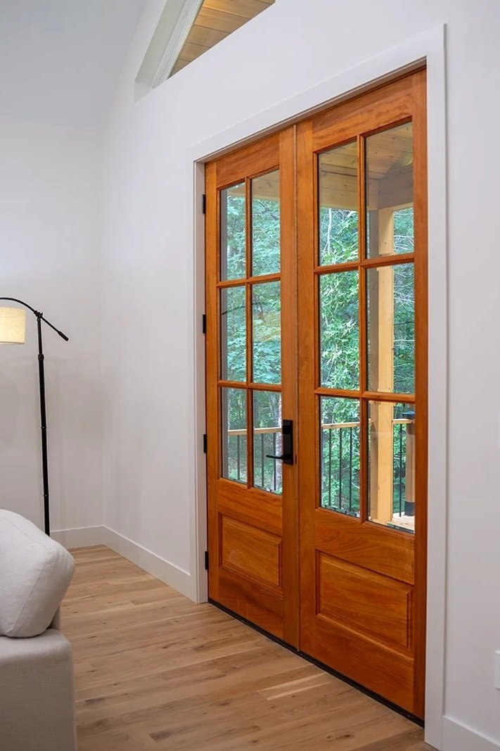 Wooden double glass-paneled door leading to an outdoor balcony with trees visible outside.