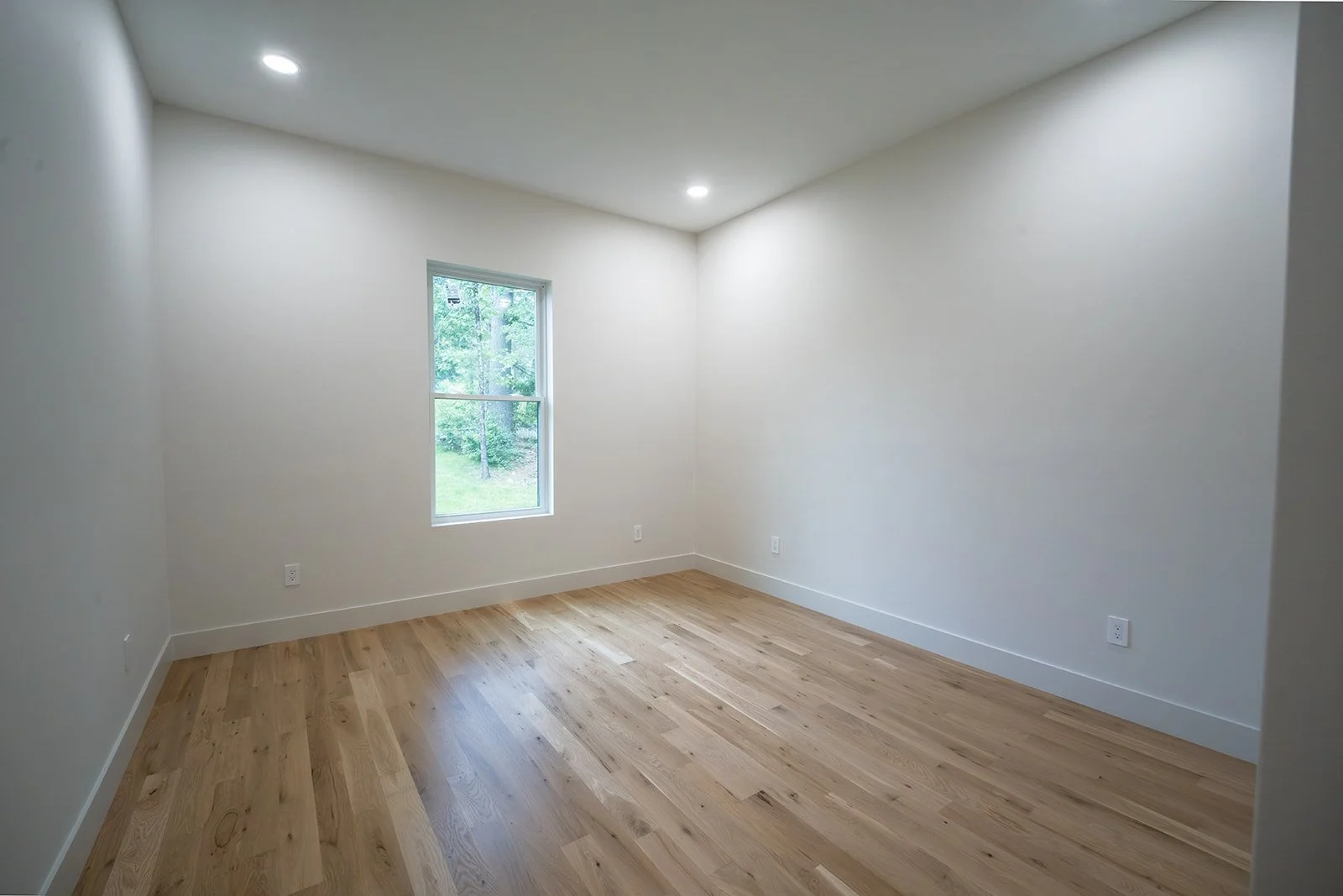 Second bedroom with white oak flooring, recessed lighting and views of the wooded setting.