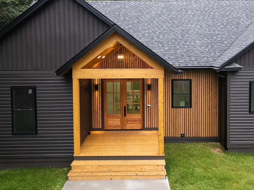 Front entrance of 20 Merrifield Road featuring natural wood accents, black siding and double glass entry doors.