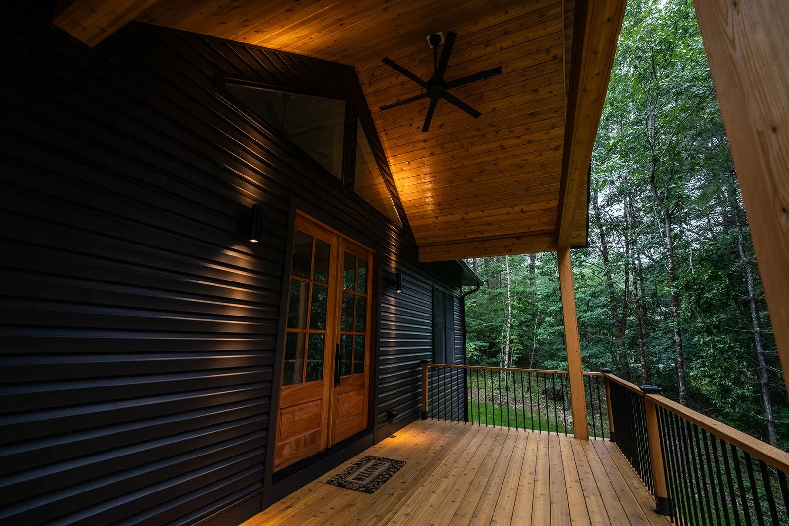 Covered porch at 20 Merrifield Road with natural wood decking, black siding and views of the surrounding woods.