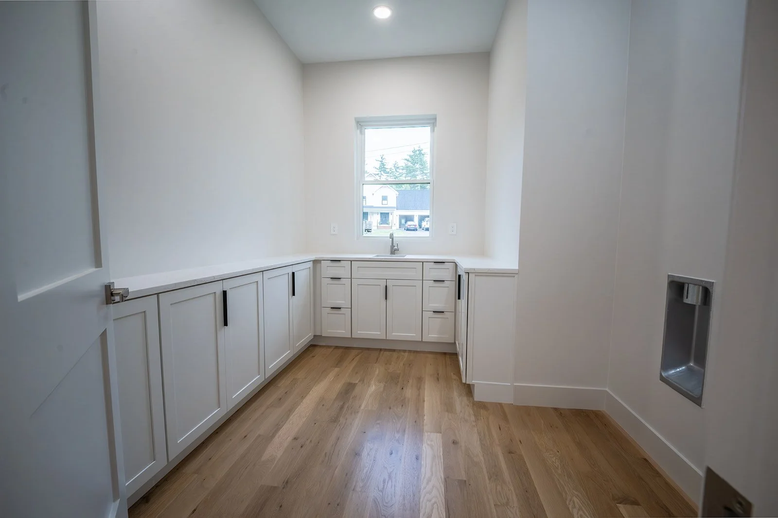 Dedicated laundry room with extensive cabinetry, countertop workspace, white oak flooring and natural light.