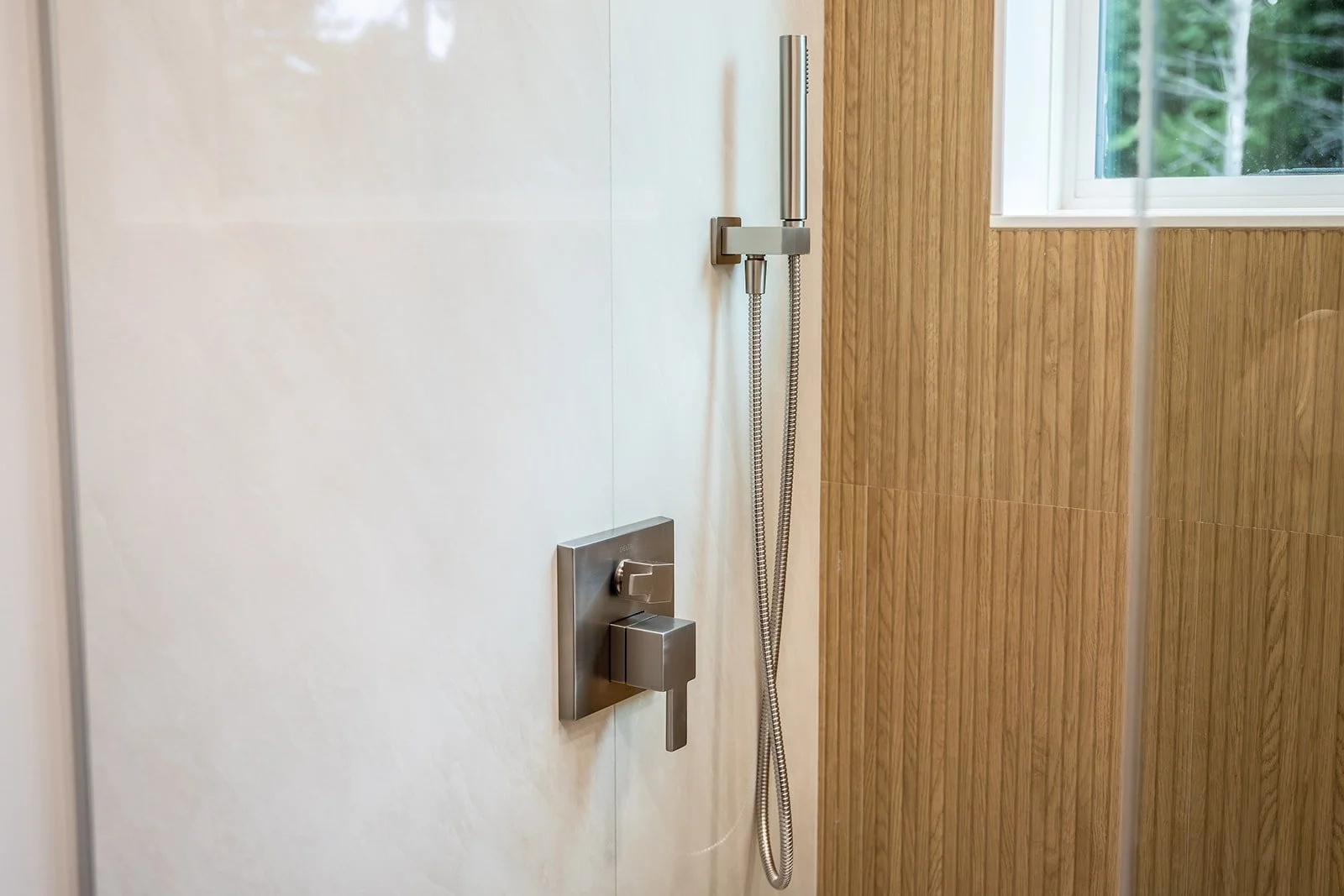Primary suite walk-in shower with rainfall fixture, modern controls and wood-look tile.