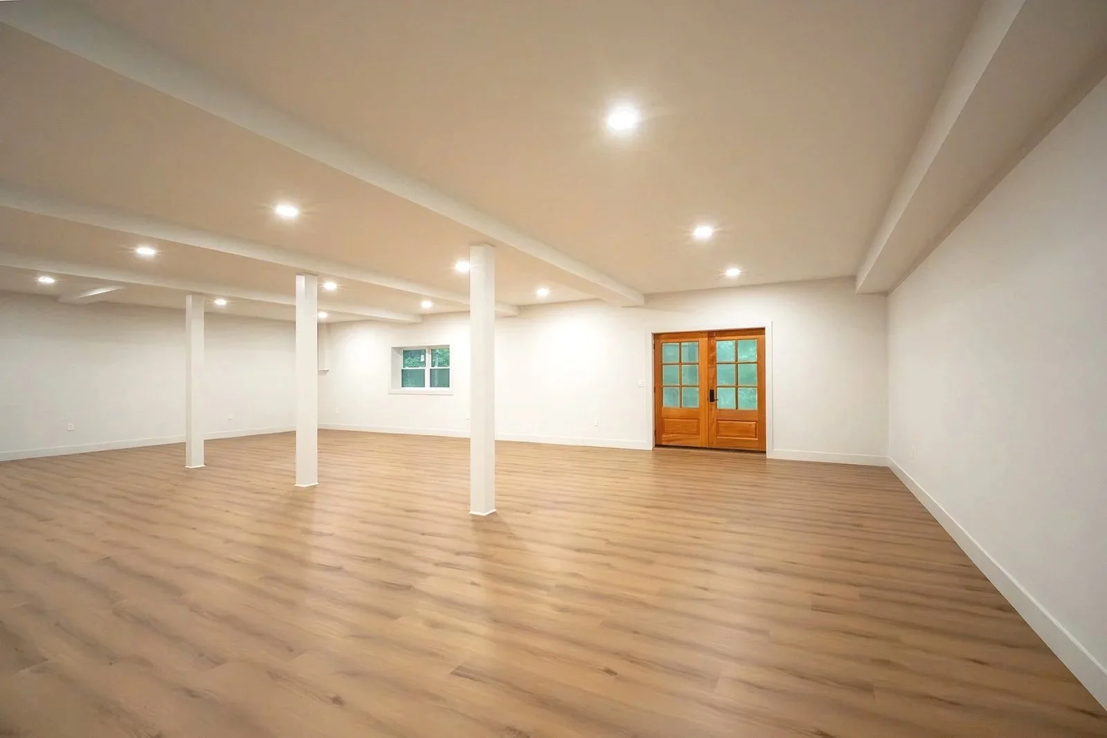 Expansive finished lower-level living space with white oak flooring, recessed lighting and exterior access.