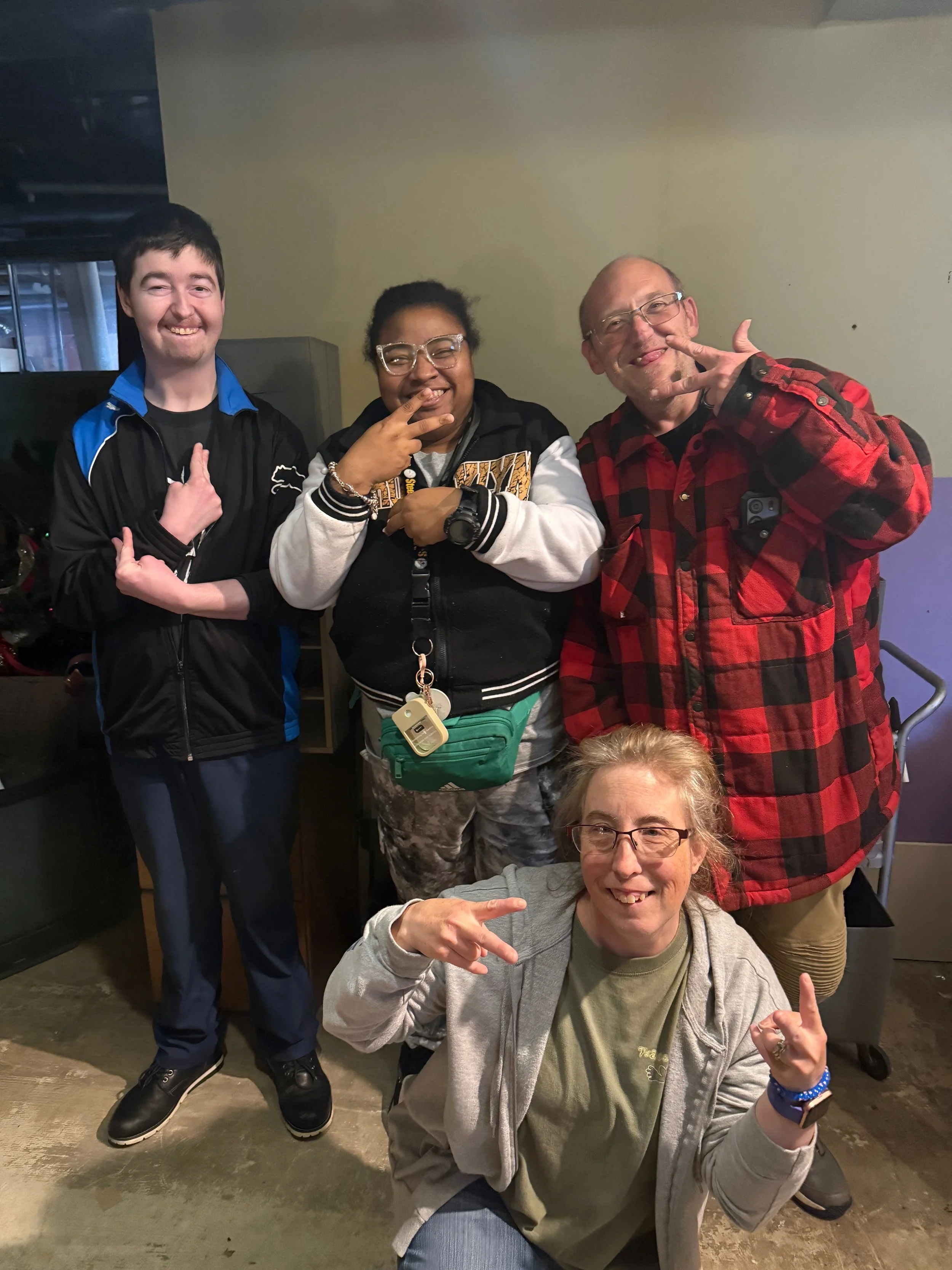 A group of four joyful people posing together indoors, making playful gestures and smiling at the camera.