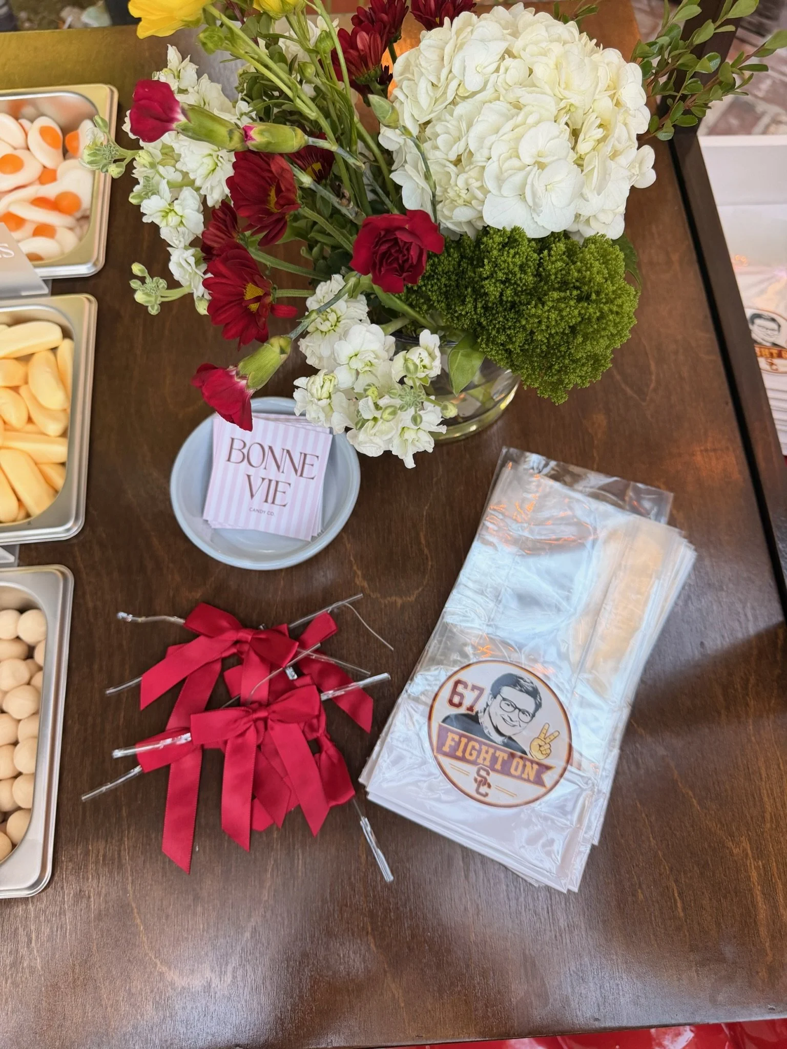 man on sticker on bag with flowers on a brown counter top and red bows with bonne vie business cards