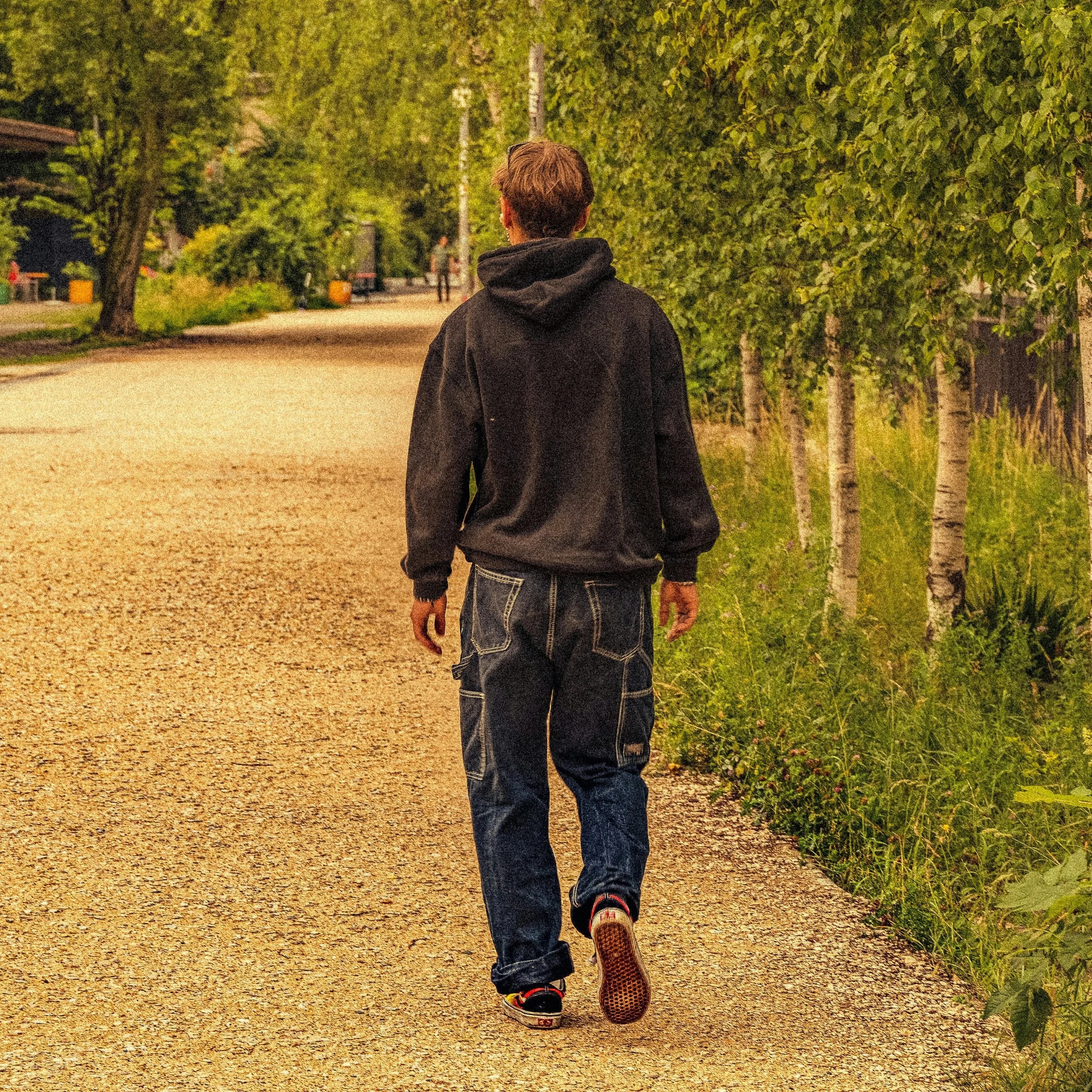 A person walking on a gravel path surrounded by lush green trees during the evening or night.