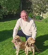 Man kneeling outdoors with two puppies on grass