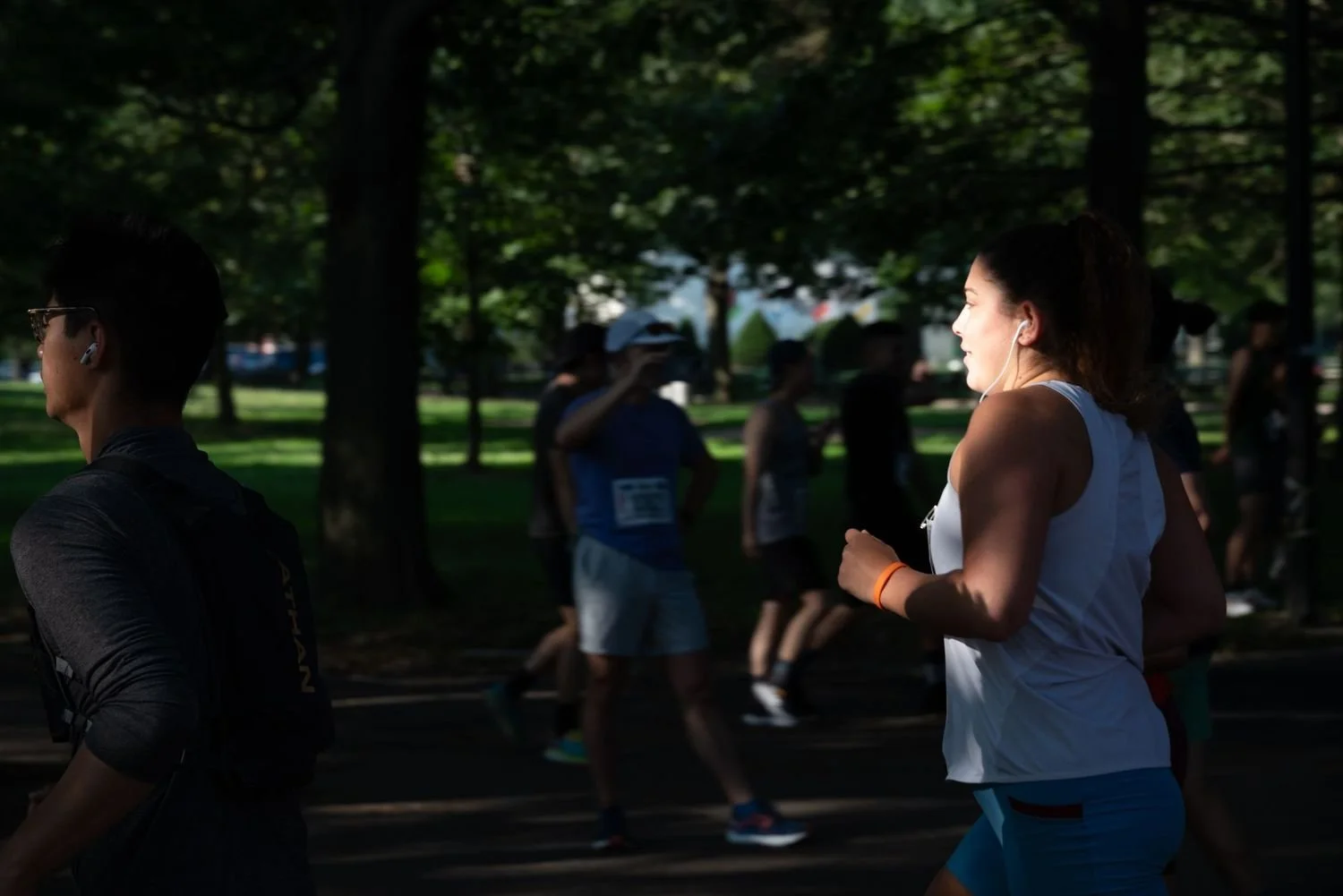 Women running in a park during a race or marathon, with others blurred in the background and trees providing shade.