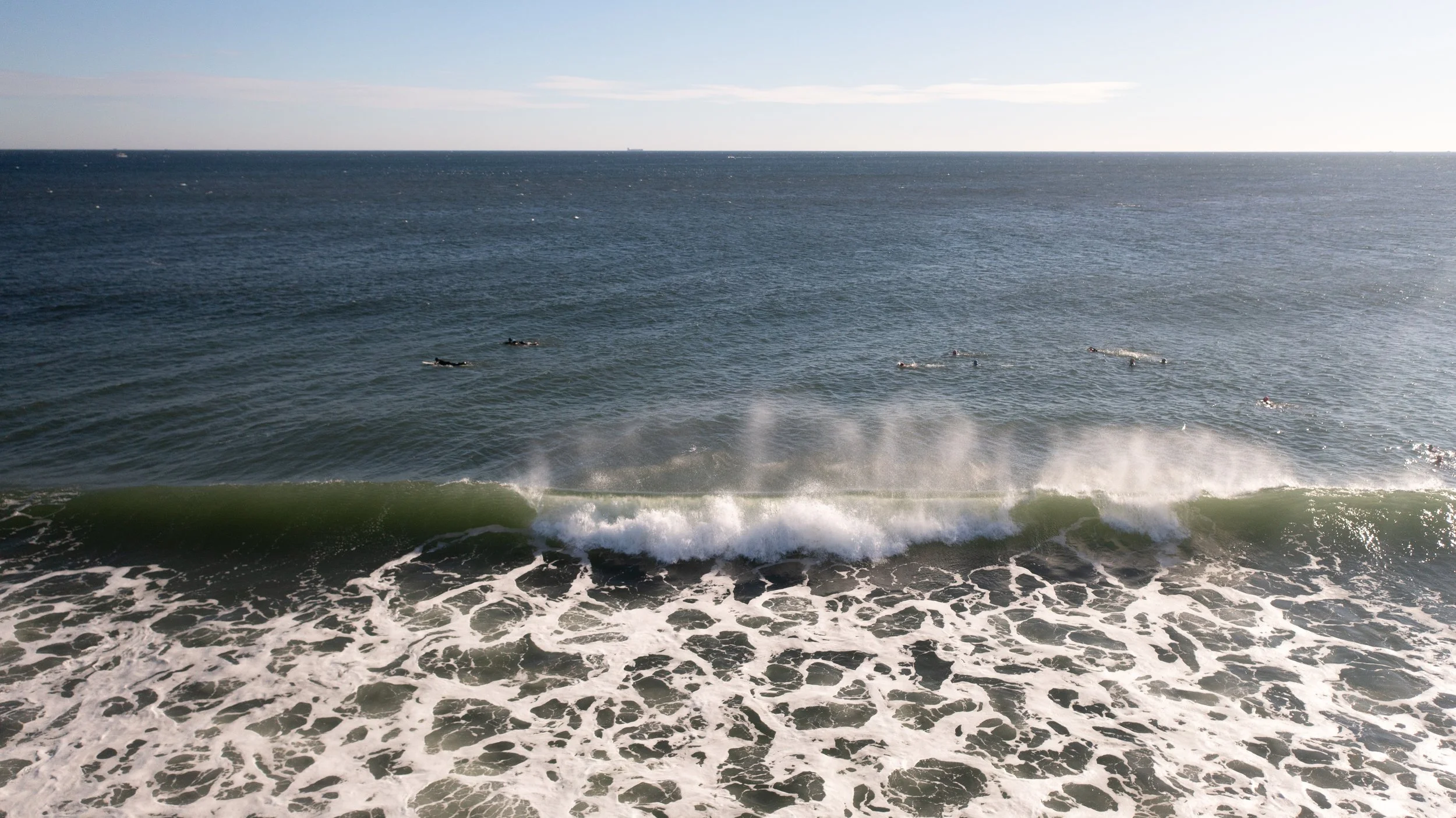 View of the ocean with small waves and surfers in the water on a clear day.