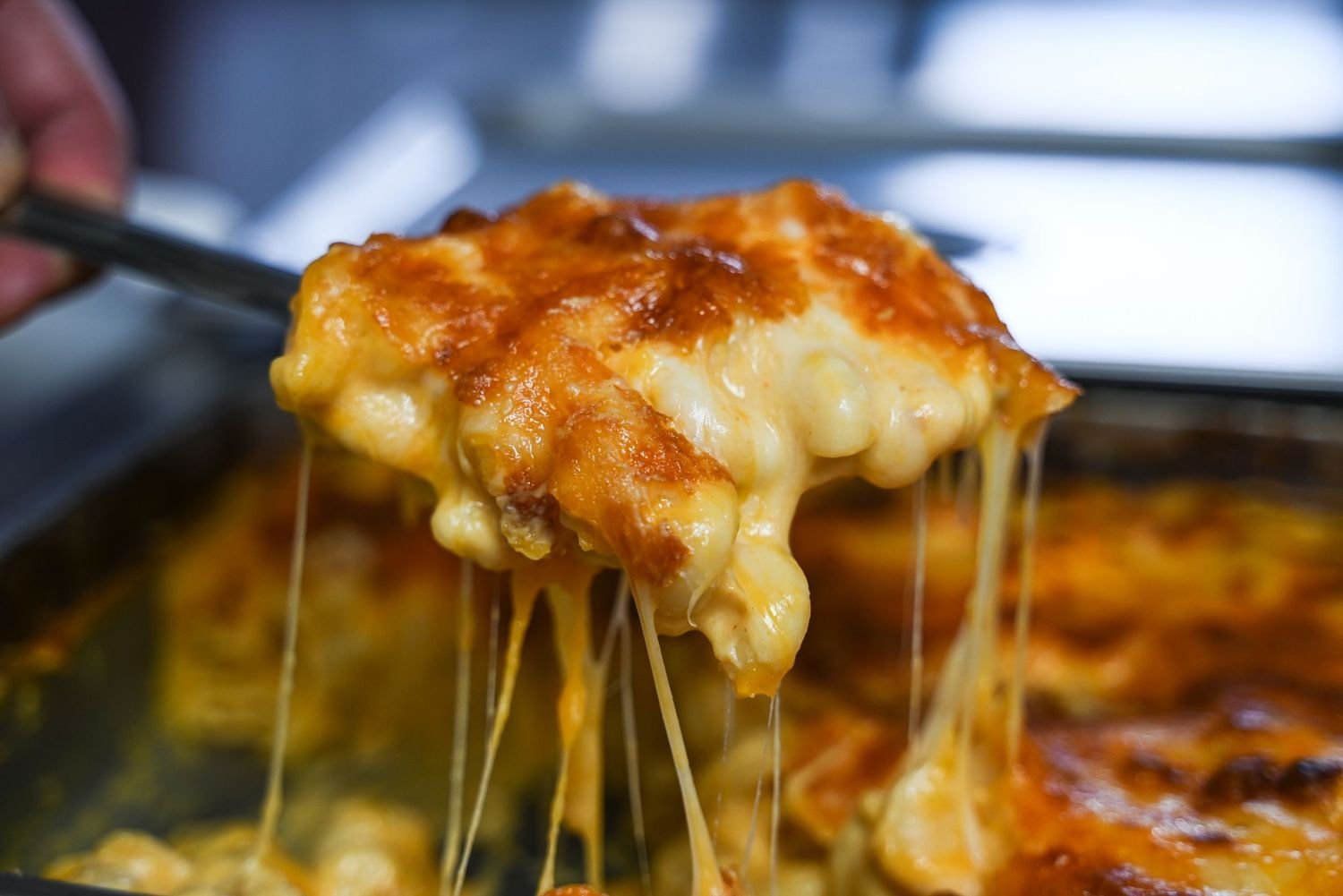 A close-up of a spoon lifting a portion of cheesy baked lasagna with melted cheese stretching in strings.