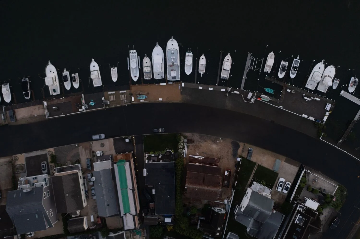 An aerial view of a marina with boats docked along the water, and residential houses in the foreground.