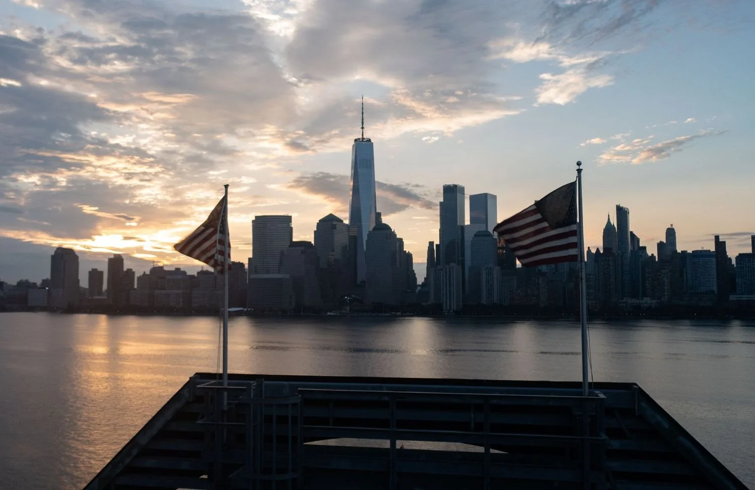 Sunset over Manhattan skyline with two American flags on a dock in the foreground.
