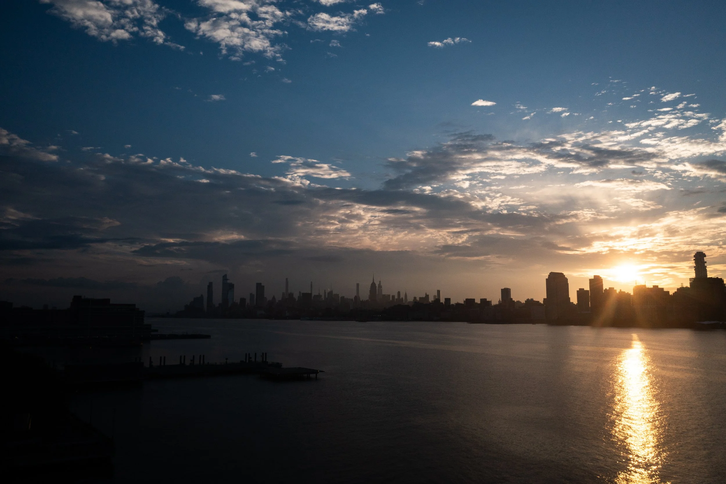 Sunset over a city skyline with high-rise buildings and a body of water in the foreground.