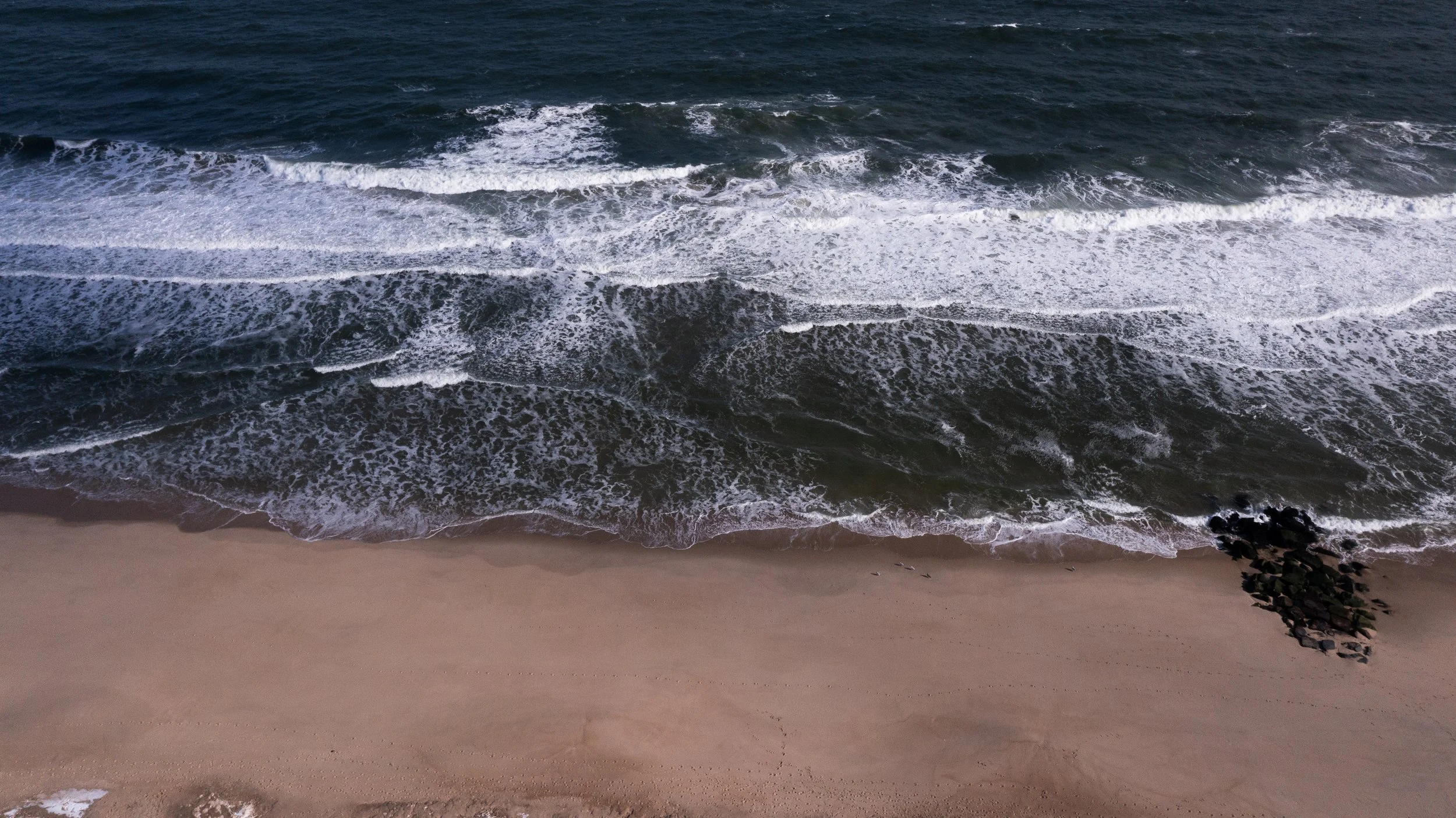 A sandy beach with small rocks at the edge, and ocean waves crashing onto the shore.