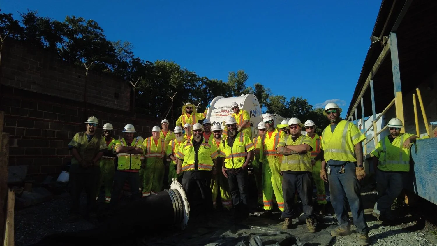 Group of construction workers and engineers wearing safety helmets and reflective vests at a construction site during daytime.