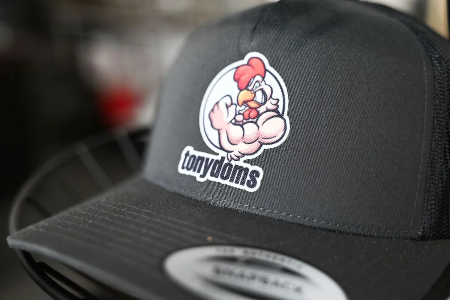 Black cap with a cartoon chicken flexing its arm and the word "tonytoms" underneath.