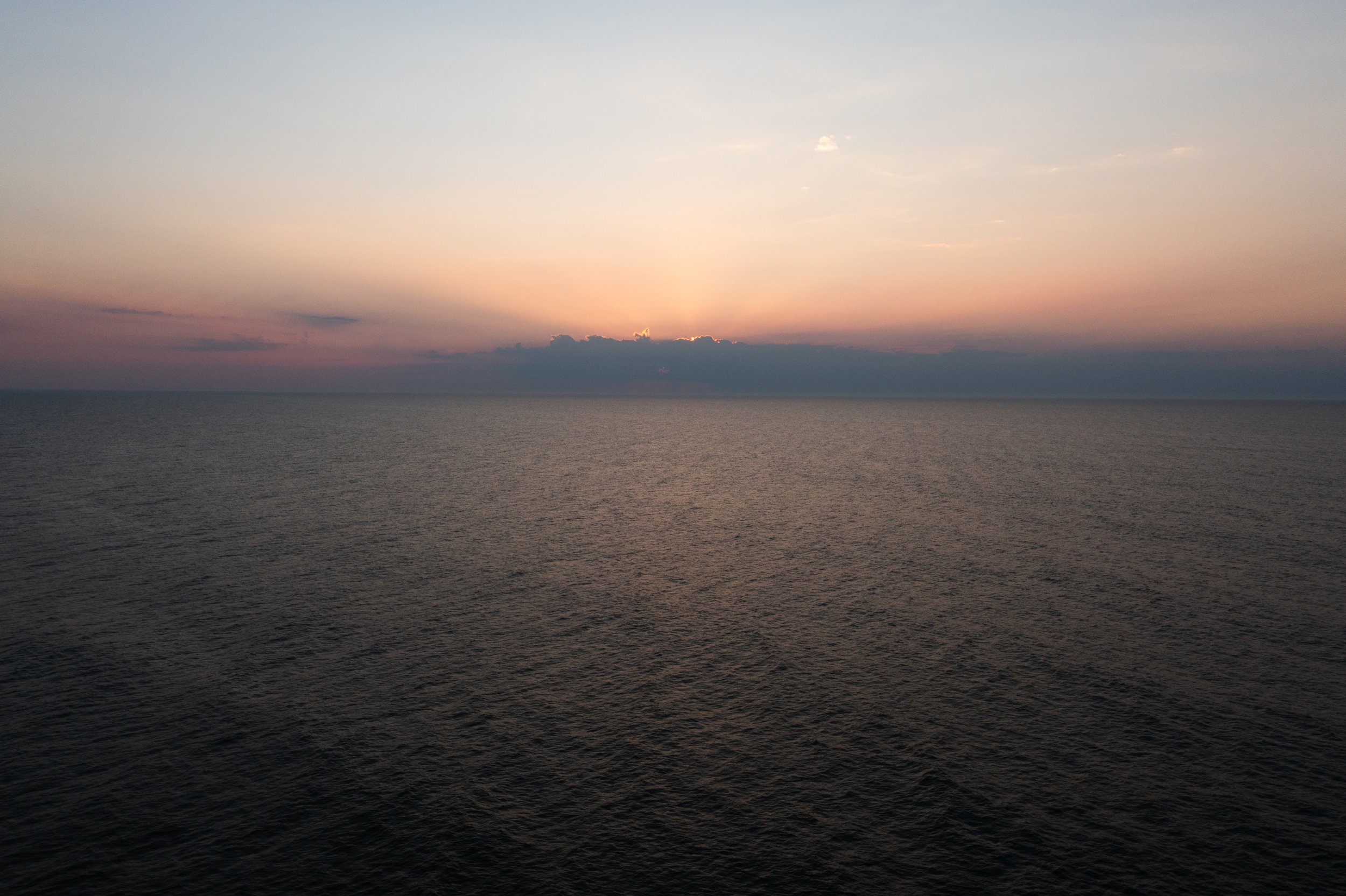Sunset over the ocean with a cloud formation near the horizon.