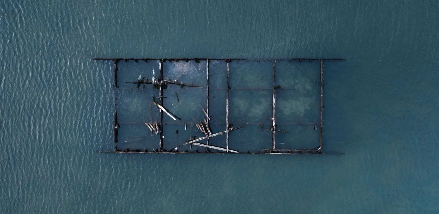 Aerial view of a sunken shipwreck in a body of water, with visible broken sections and debris.