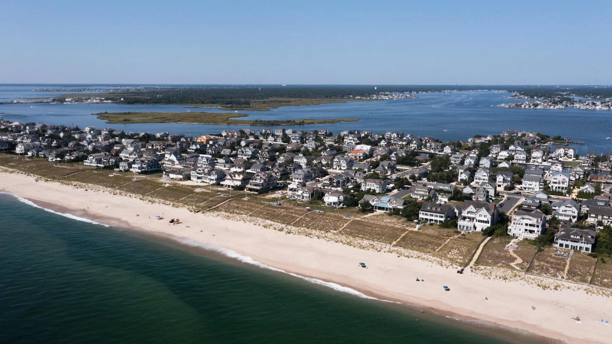 Aerial view of a coastal neighborhood with beach, houses, and waterway.