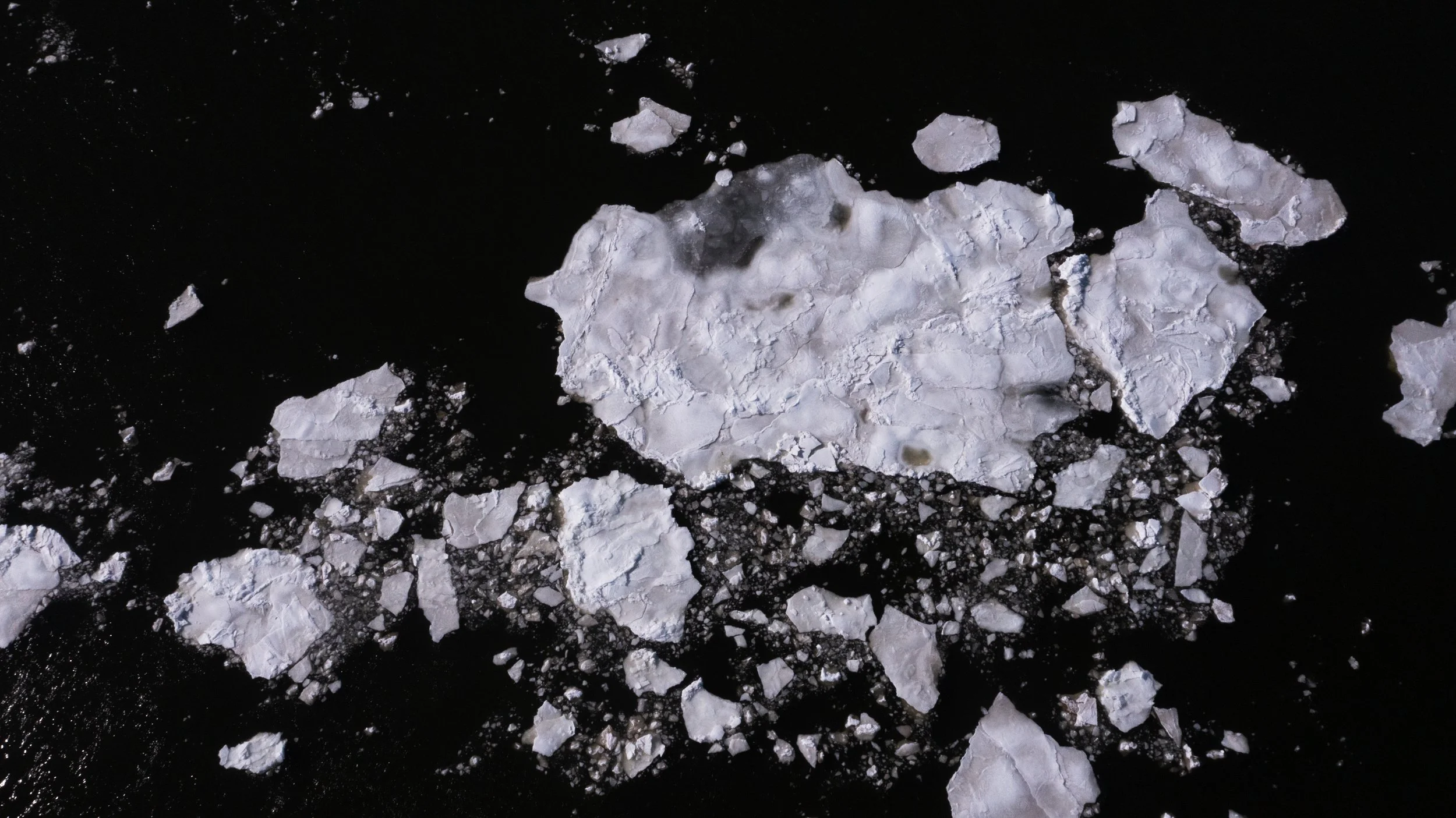 Broken white ice chunks floating in dark water.