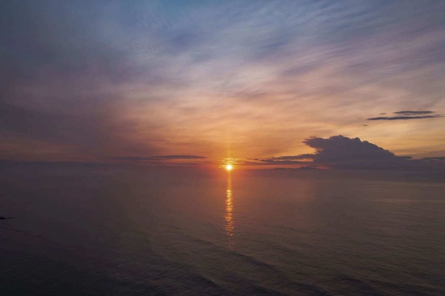 Sunset over calm ocean waters with clouds in the sky.