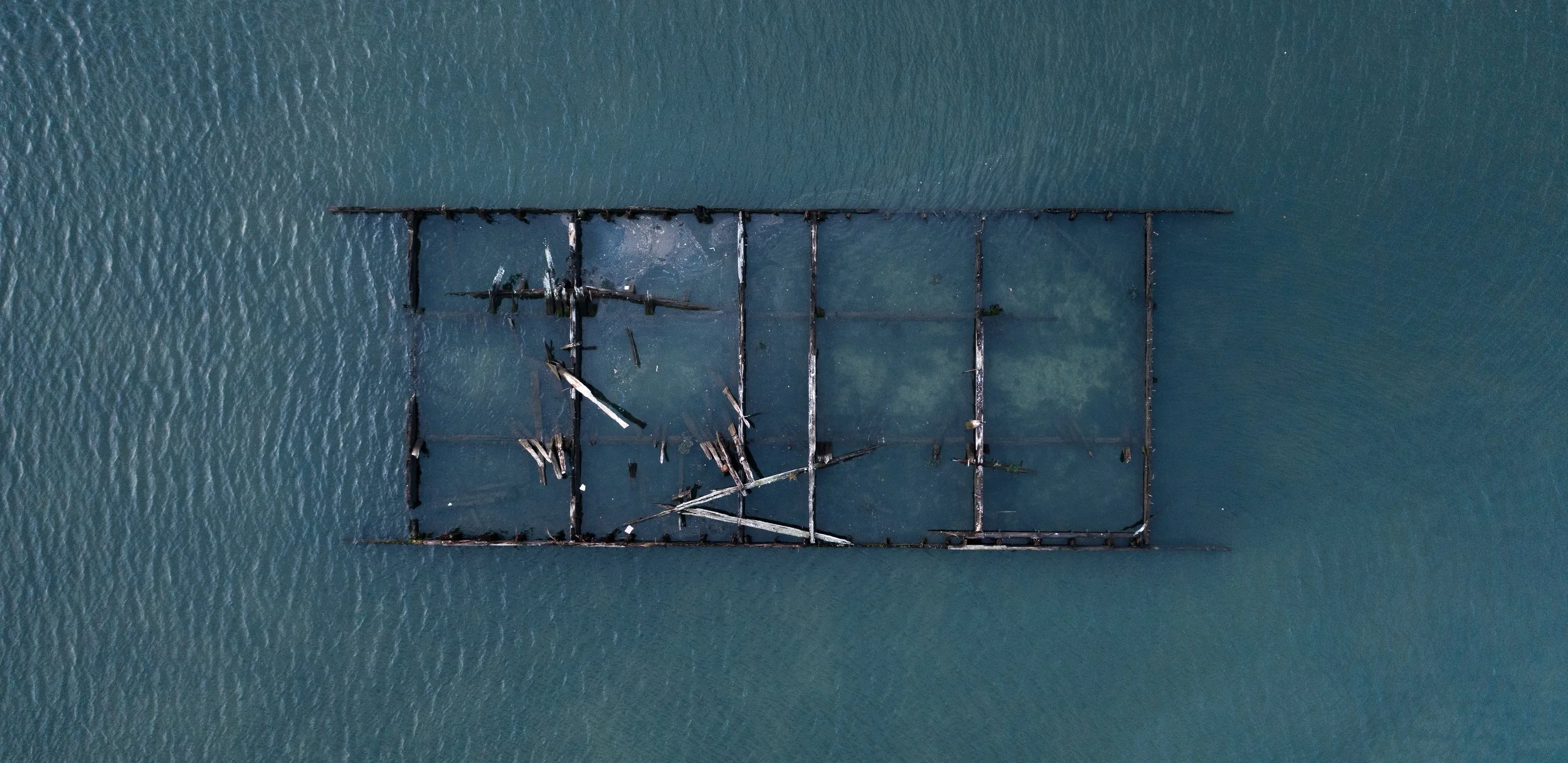 Aerial view of a sunken shipwreck in the water, with some broken beams and debris visible.