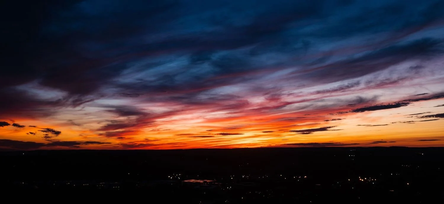 Colorful sunset sky with dark clouds over a landscape with small lights.