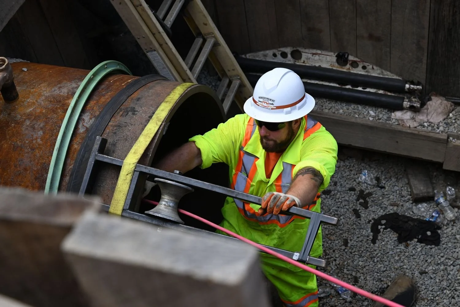 Construction worker in bright yellow safety gear and white helmet working on large underground pipe at a construction site.