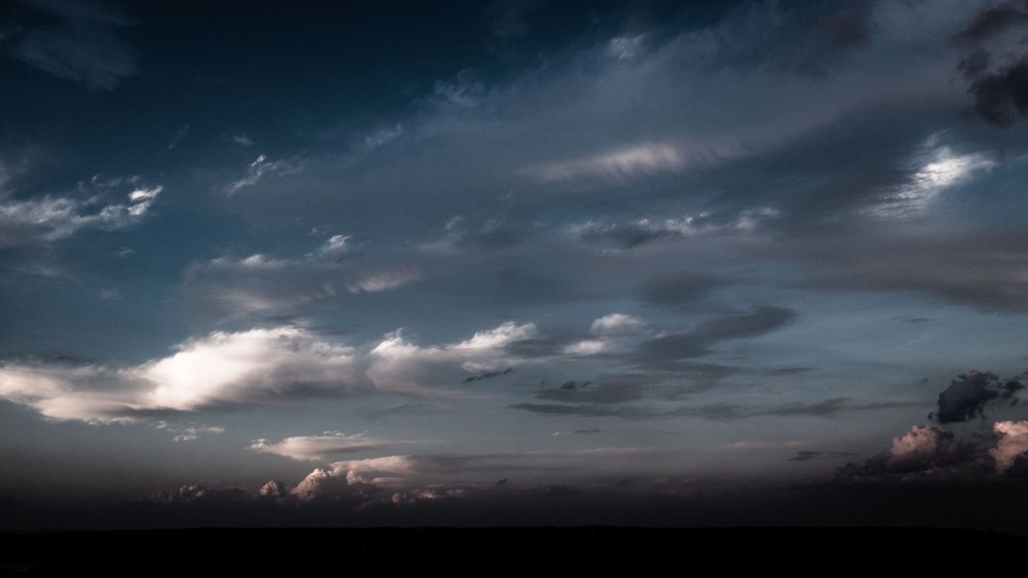 Cloudy sky at dusk with dark clouds and a faint hint of light near the horizon.