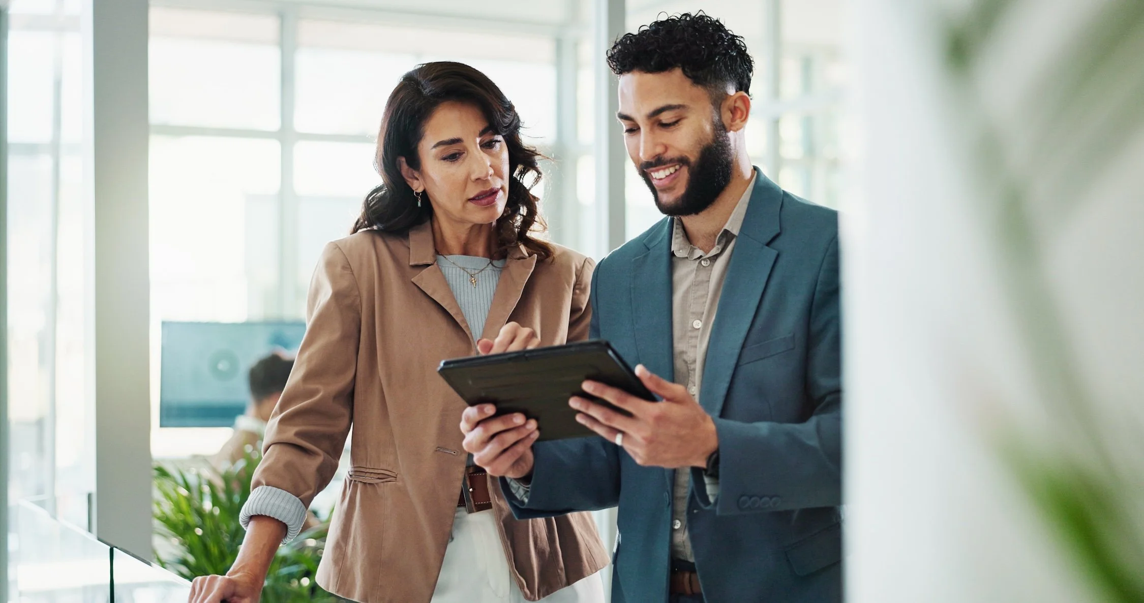 A man and a woman are looking at a tablet together in an office setting.