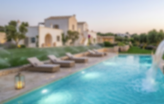 Piscina esterna con lettini al tramonto, su uno sfondo di case bianche e vegetazione.