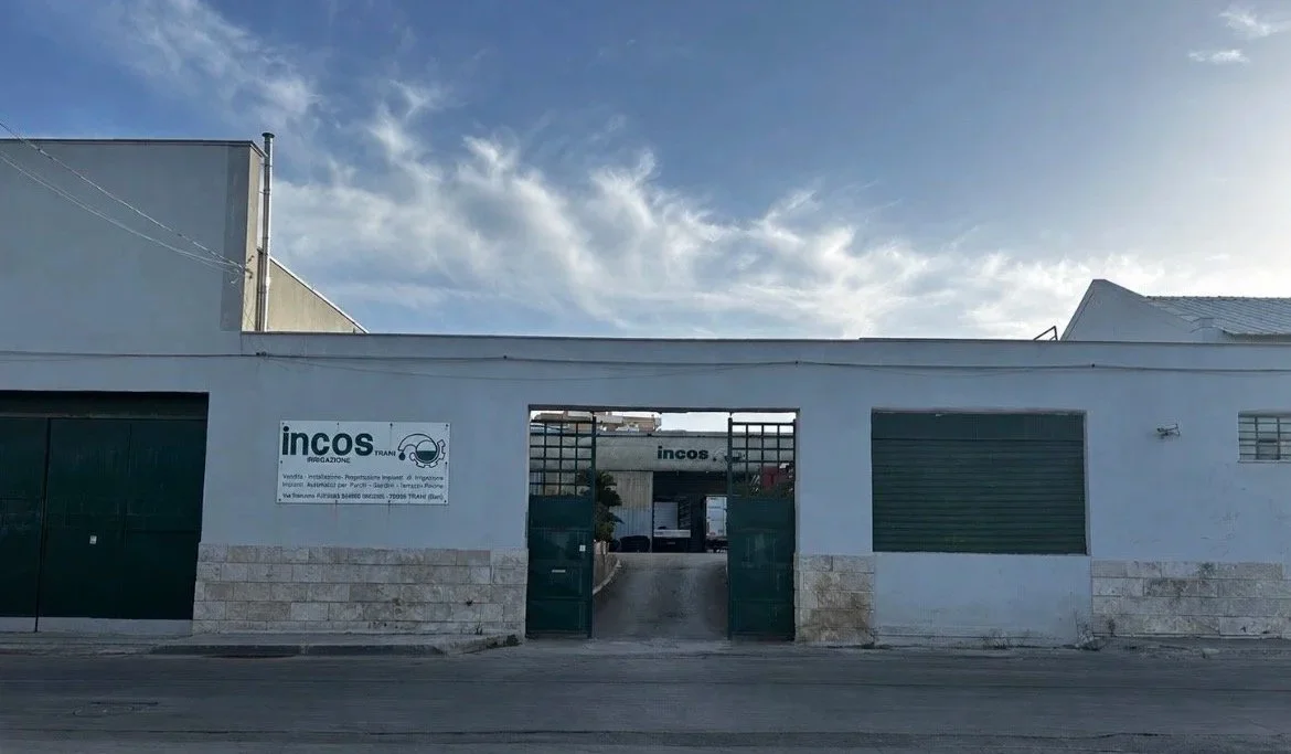 Vista dell'ingresso di un complesso industriale con due cancelli e un cartello che riporta il nome 'incos'.