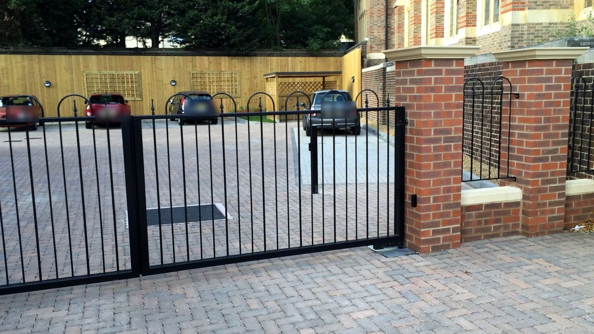 Black railed double swing gates between red brick piers at a car park entrance