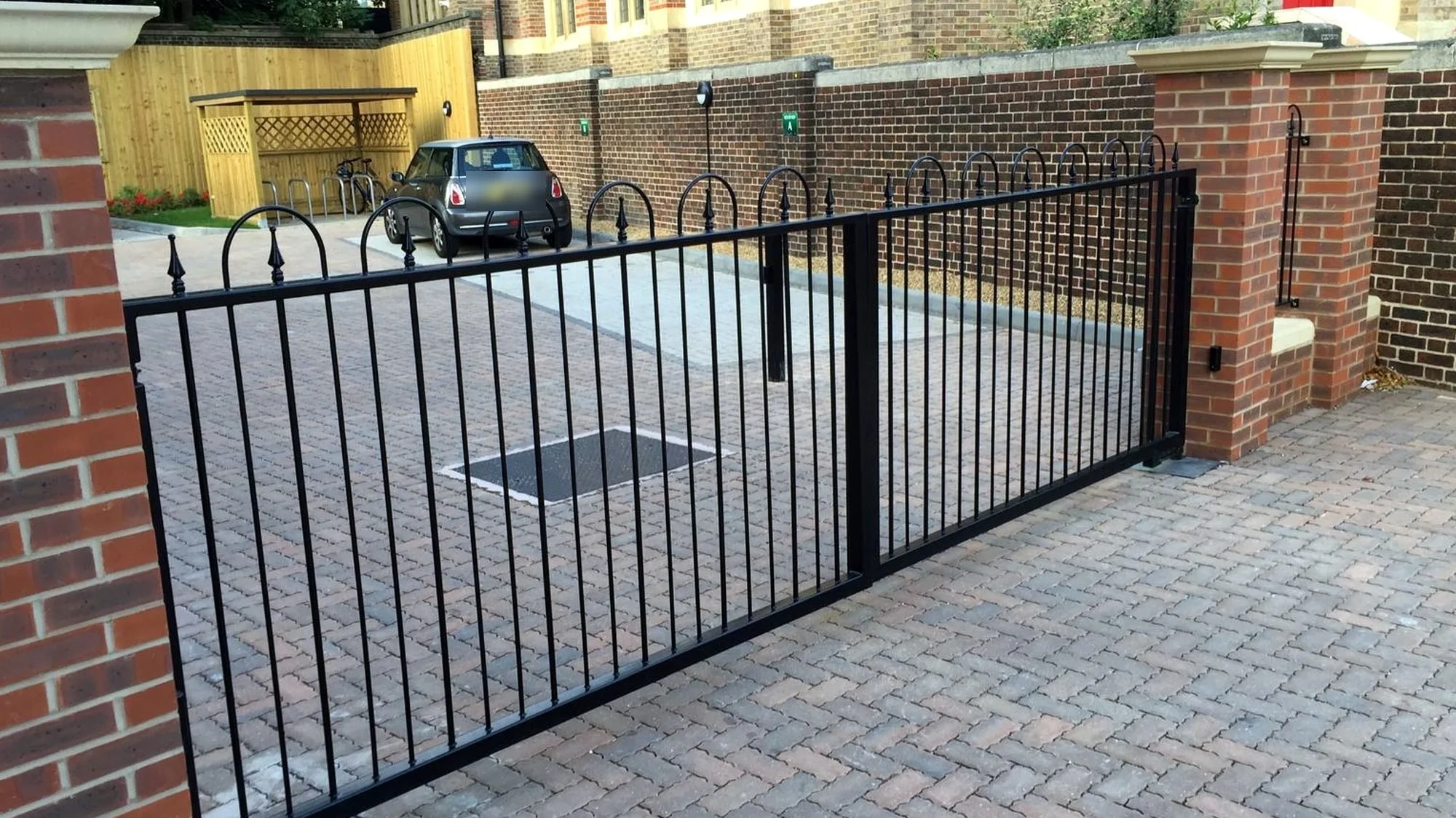 Wide view of black automated swing gates and railings on brick piers at a car park entrance