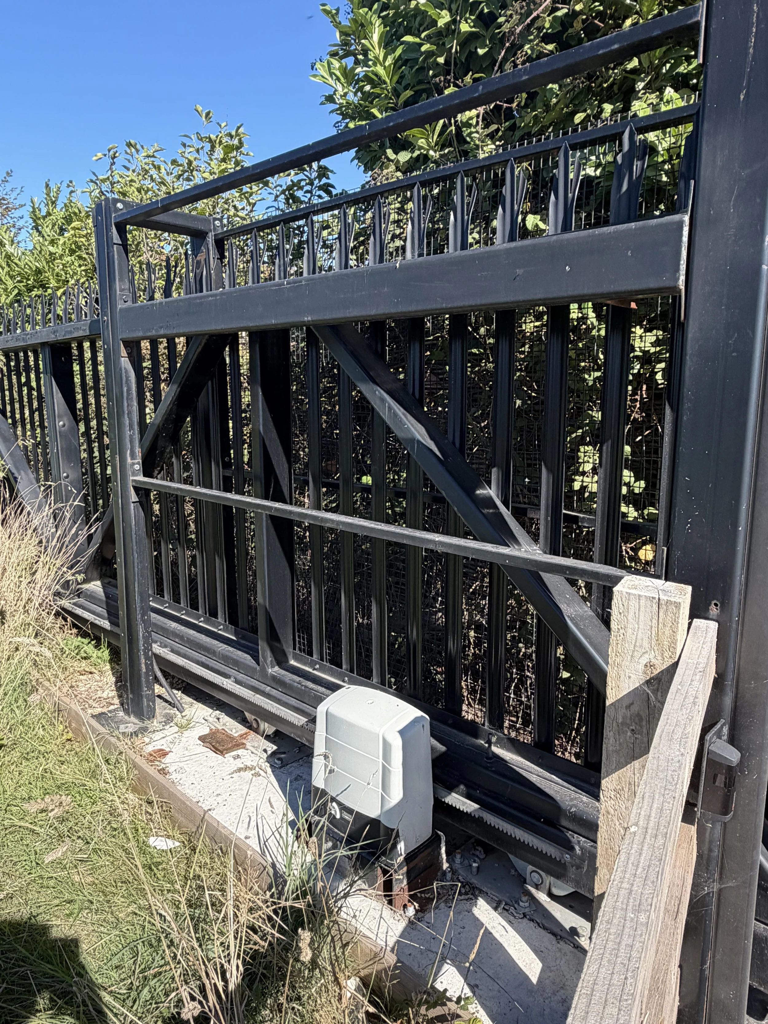 Black steel automated gate with a control box beside the post