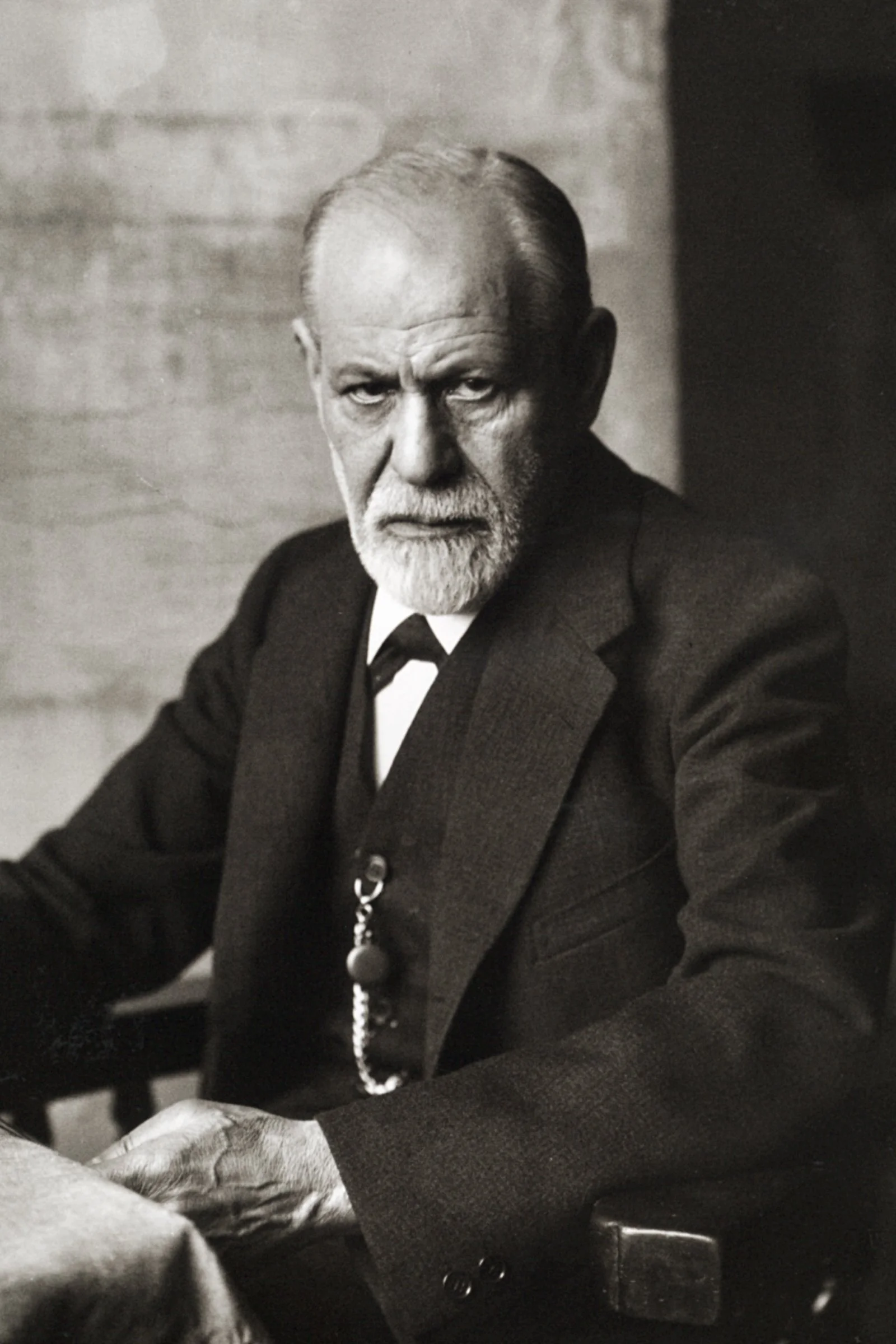 Schwarz-weiß-Foto von Sigmund Freud, der am Tisch sitzt und ernst in die Kamera blickt.