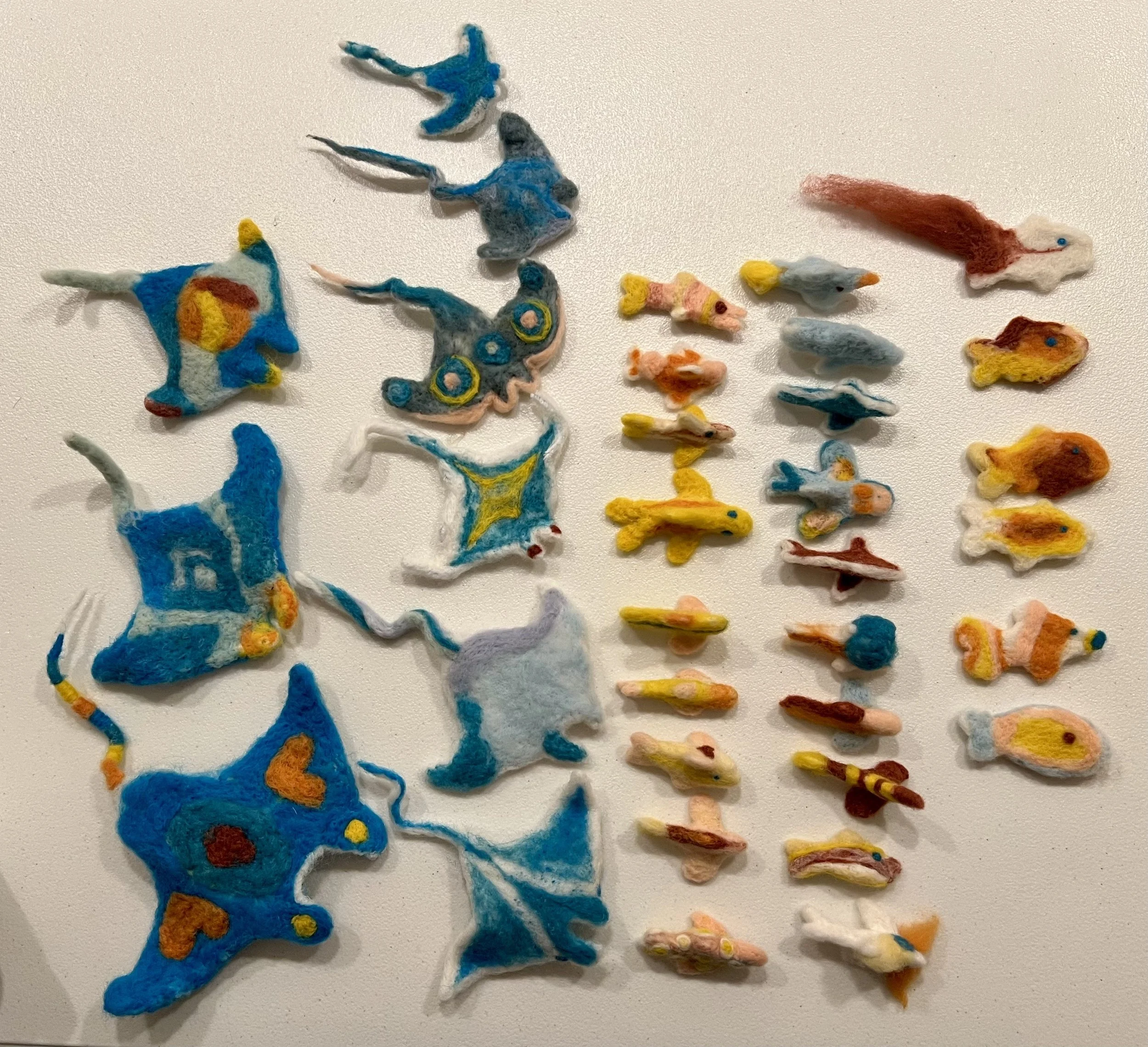 felted fish and manta rays, organized in rows, ready to be assembled