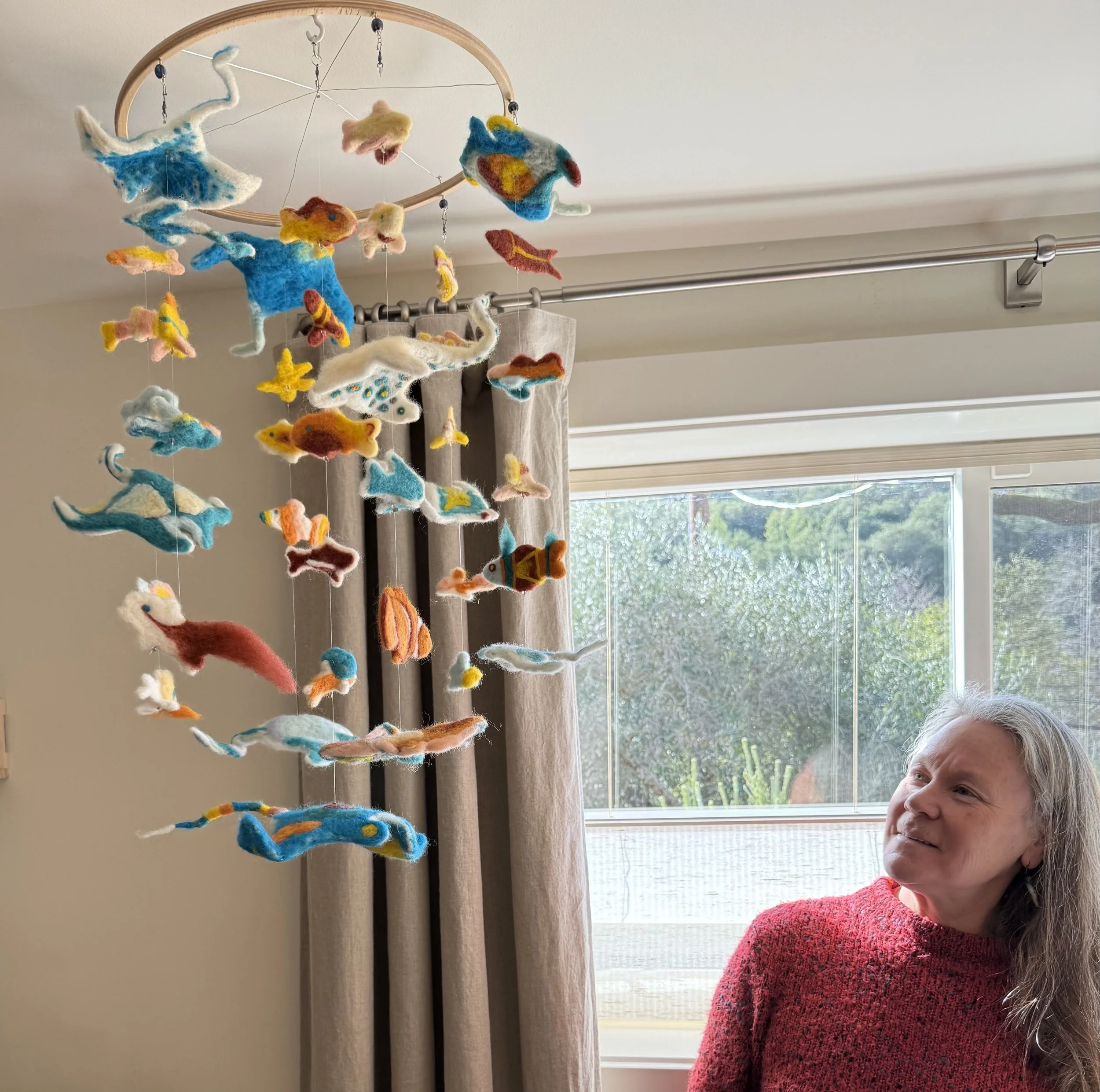 Felt fish and manta ray mobile in a baby room with the artist looking up at it