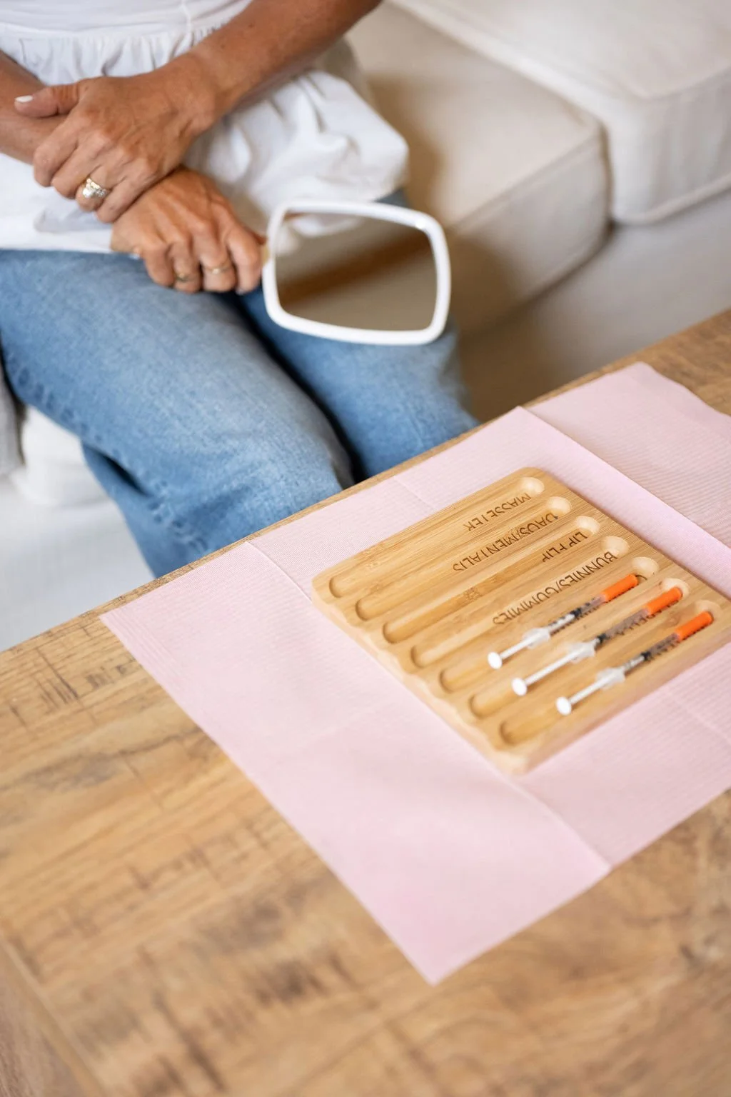 Client holding a mirror beside a tray of labeled botox syringes during an in-home treatment in Wilmington, NC