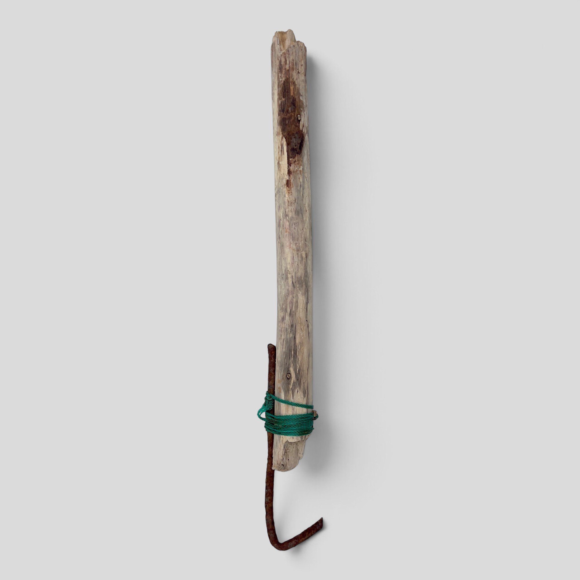 Working Object, 14, 2026: A long piece of pale, weathered wood bound with green cord to a rusted iron rod ending in a curved hook.