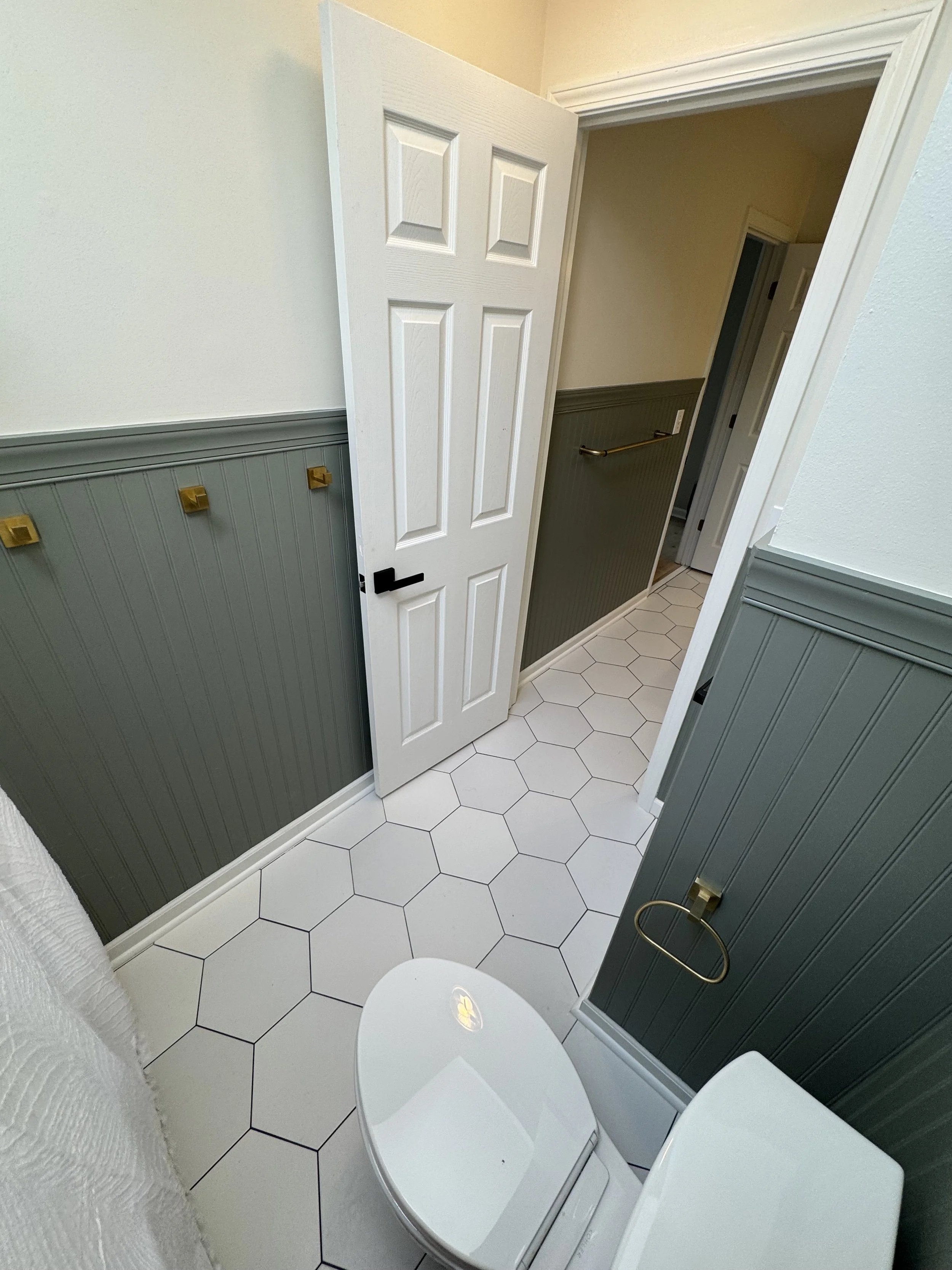 Bathroom with white hexagon tile floor, dark green wainscoting, and a white toilet.