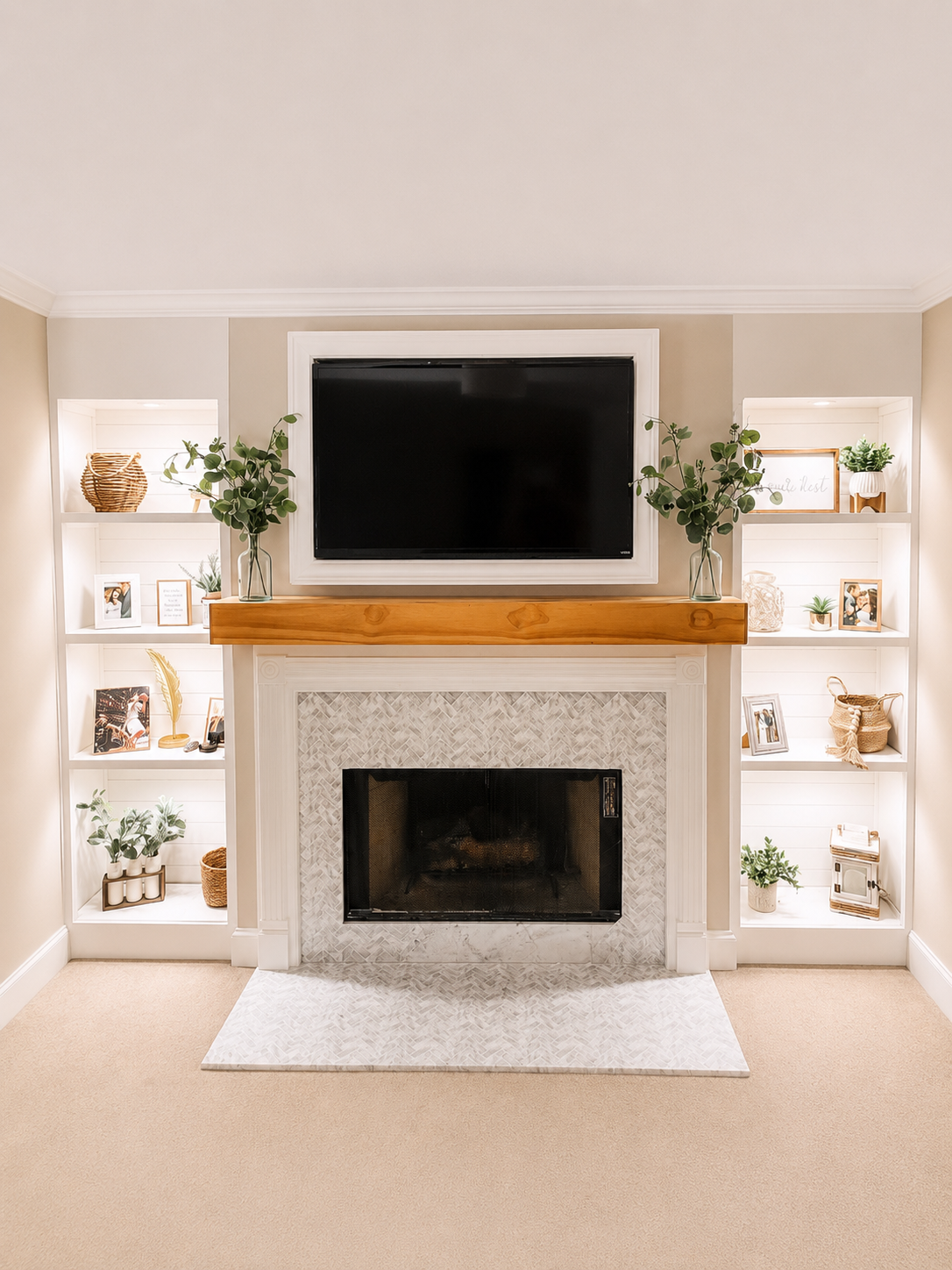 Living room fireplace with a mounted TV above it, flanked by built-in white shelves decorated with plants, picture frames, baskets, and decorative items.