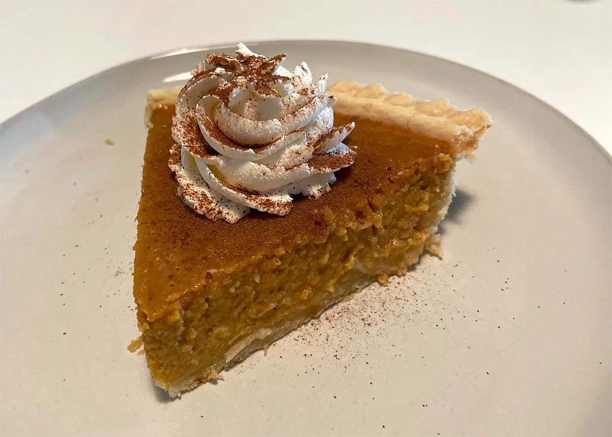 Slice of pumpkin pie topped with whipped cream and cinnamon on a white plate