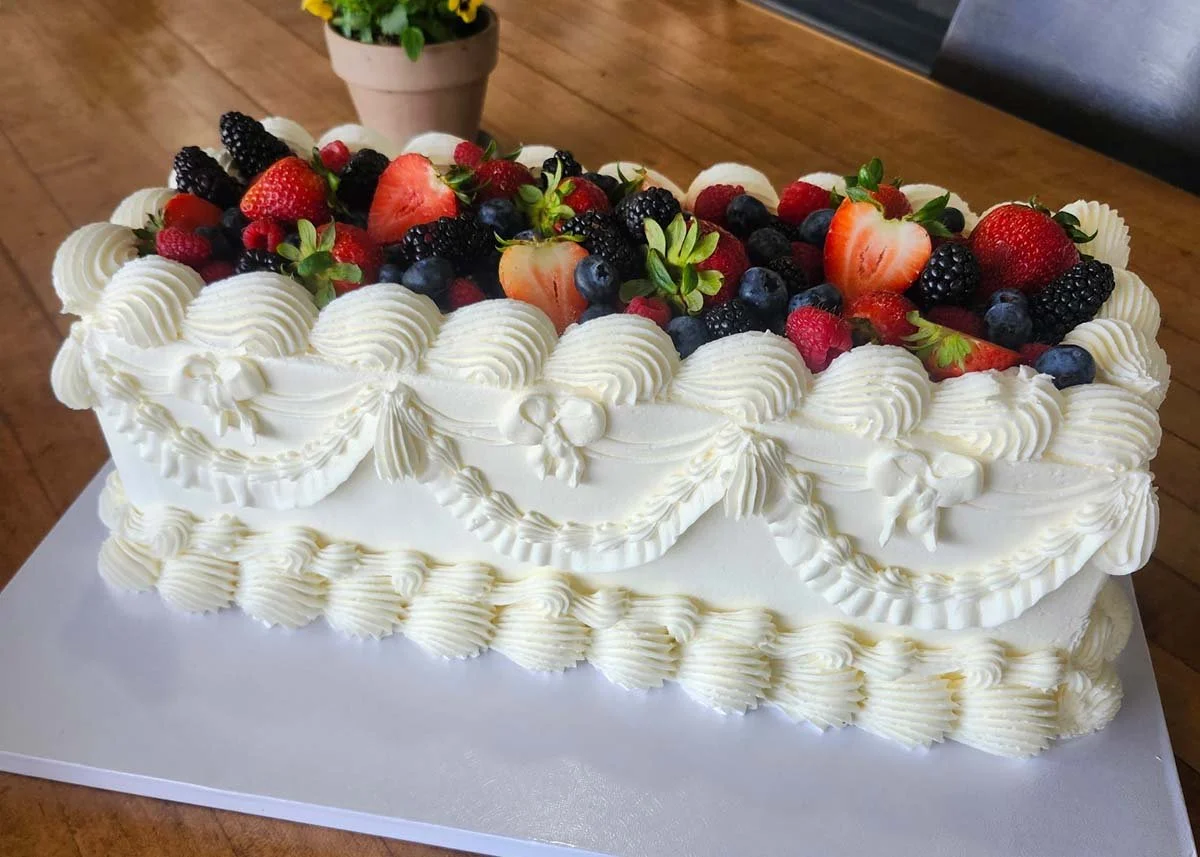 Decorated rectangular white cream cake topped with strawberries, blueberries, blackberries, and raspberries